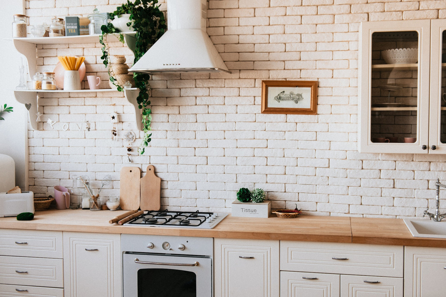 Bright white kitchen with wooden counter top and brick wall.